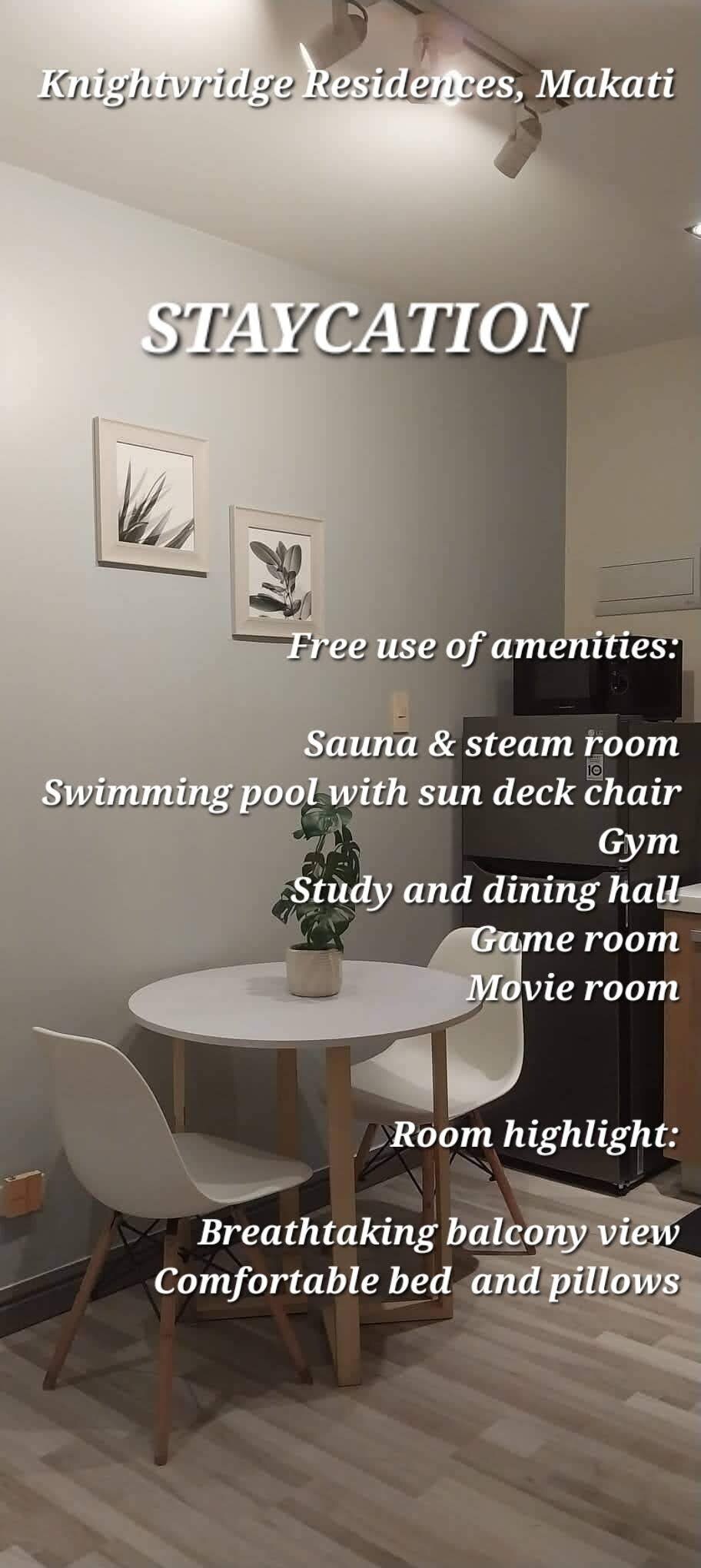 A compact dining area is showcased with a round table and two chairs, creating a cozy setting. Framed botanical art adorns the walls, complementing the light grey color scheme. Info about complimentary amenities is presented in a clean, modern font, emphasizing a staycation experience.