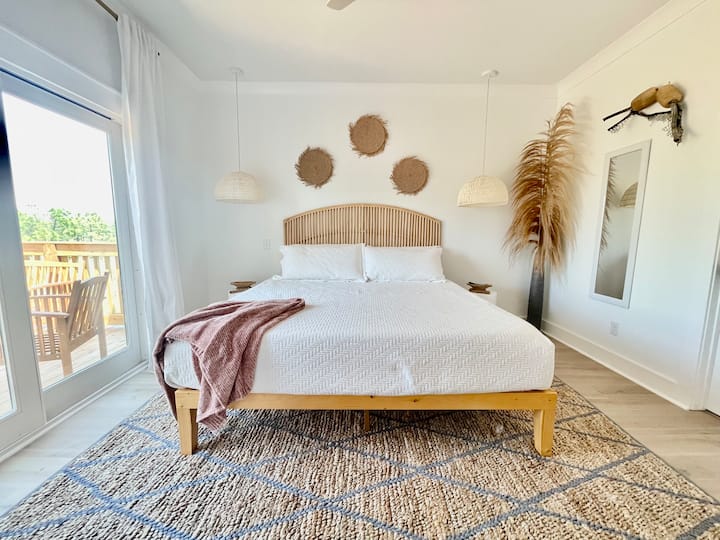 Este dormitorio principal tiene su propio baño privado en suite, una cómoda cama tamaño king de espuma viscoelástica, moderna decoración costera, una puerta corrediza a la amplia terraza trasera con vistas al mar de los humedales, que son de ensueño al atardecer.