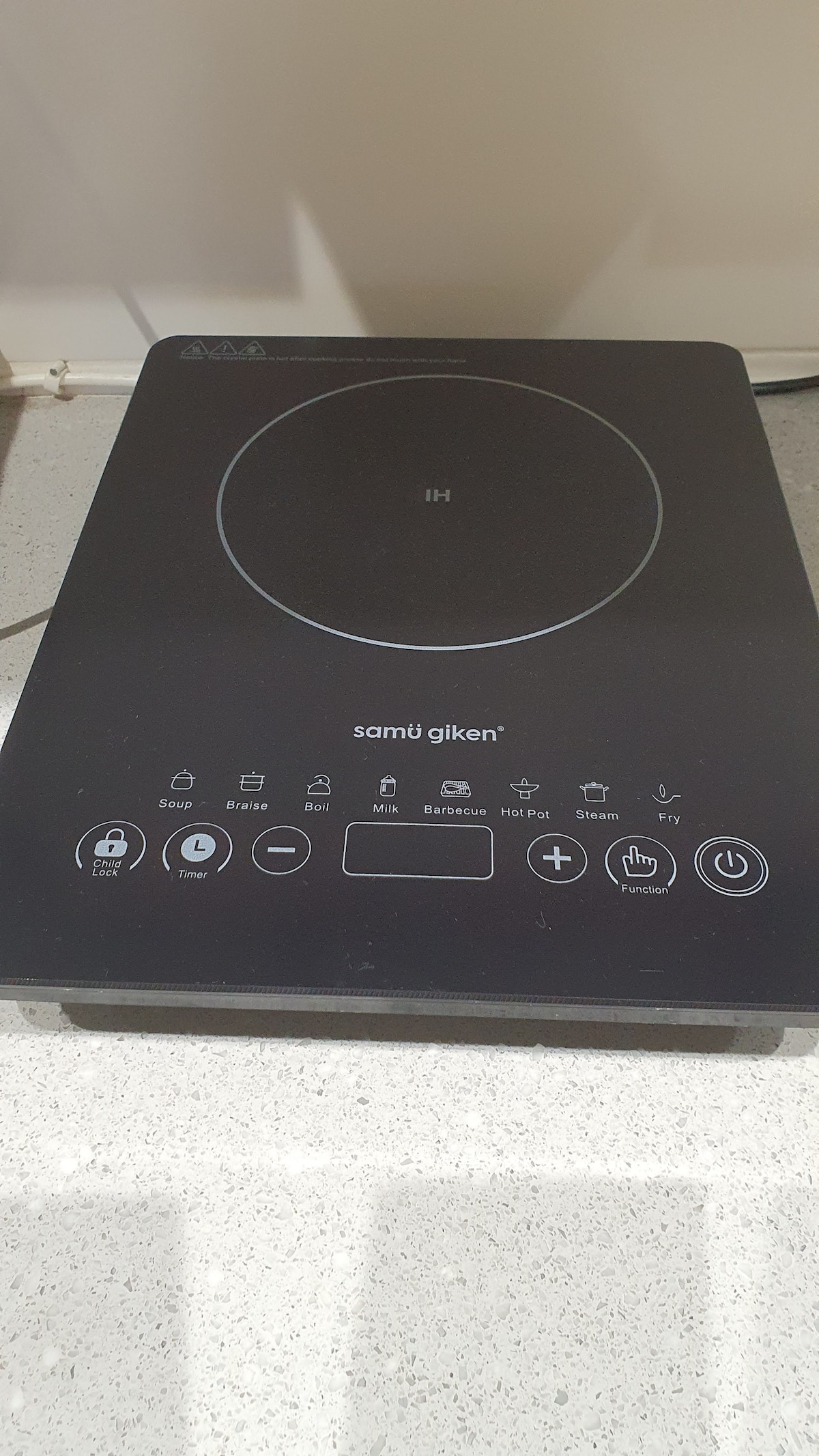 A sleek induction cooktop is displayed on a clean countertop. The surface features a minimalist design with various control buttons for cooking settings, prominently featuring a circular cooking area at the center, contributing to a modern kitchen aesthetic.