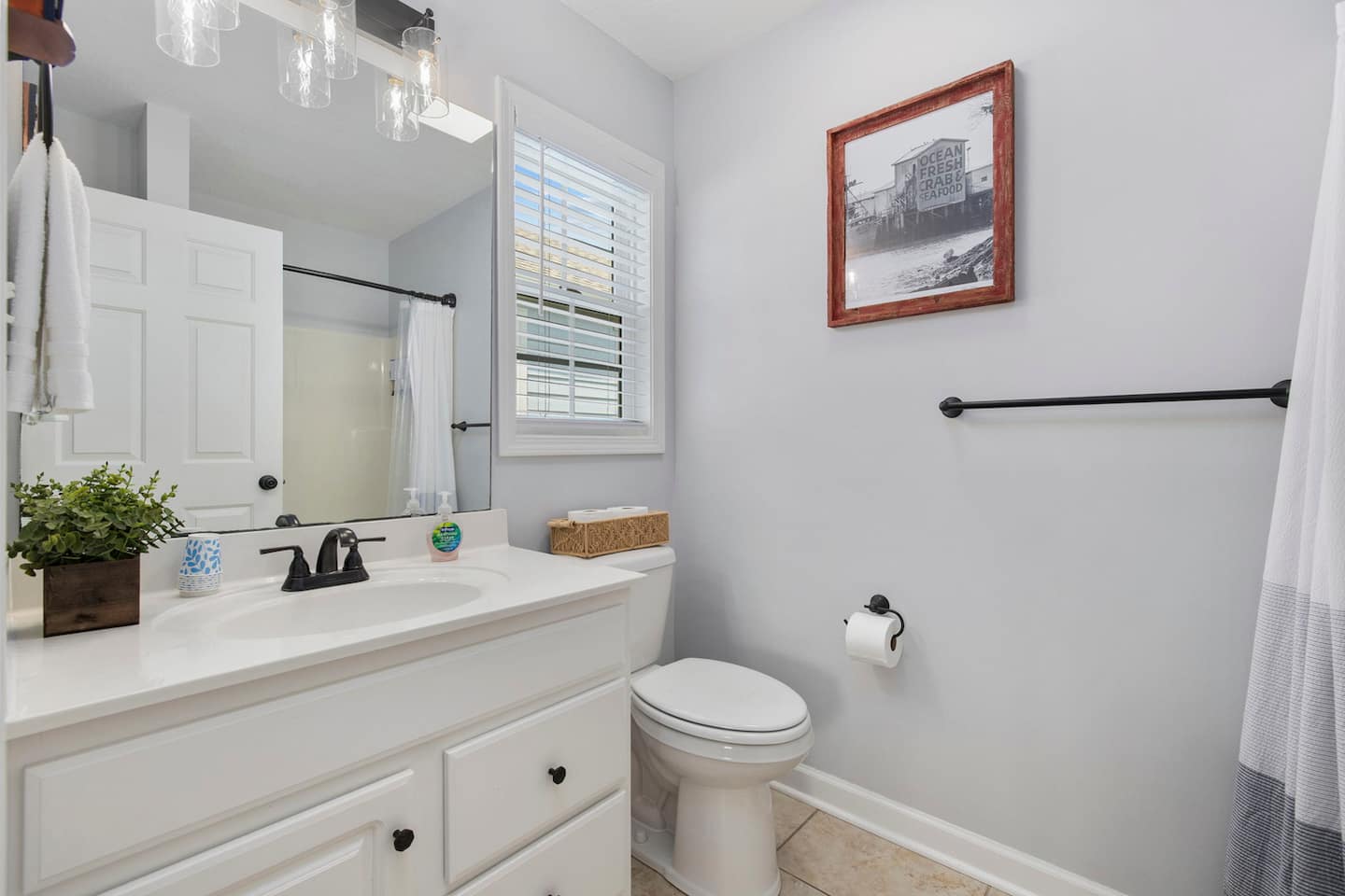 Use the in-suite bathroom: white vanity, black fixtures, and seafood market art that fits the coastal theme running through the whole house.