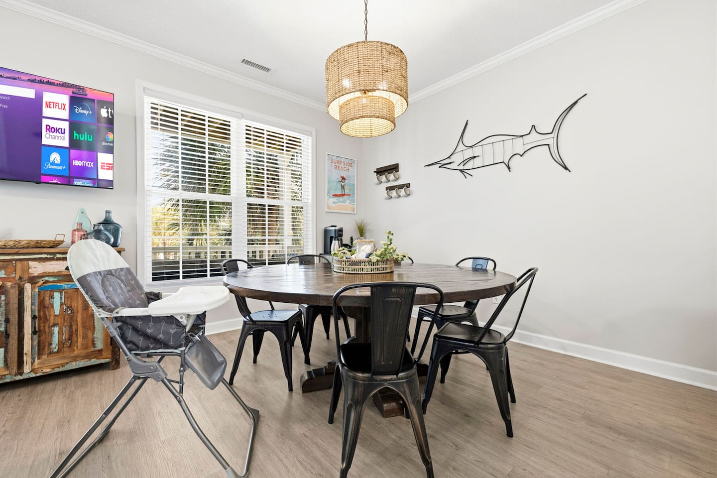 Seat the whole crew at the round dining table for a real group dinner. Wicker pendant light above, marlin on the wall, smart TV if sports is on.