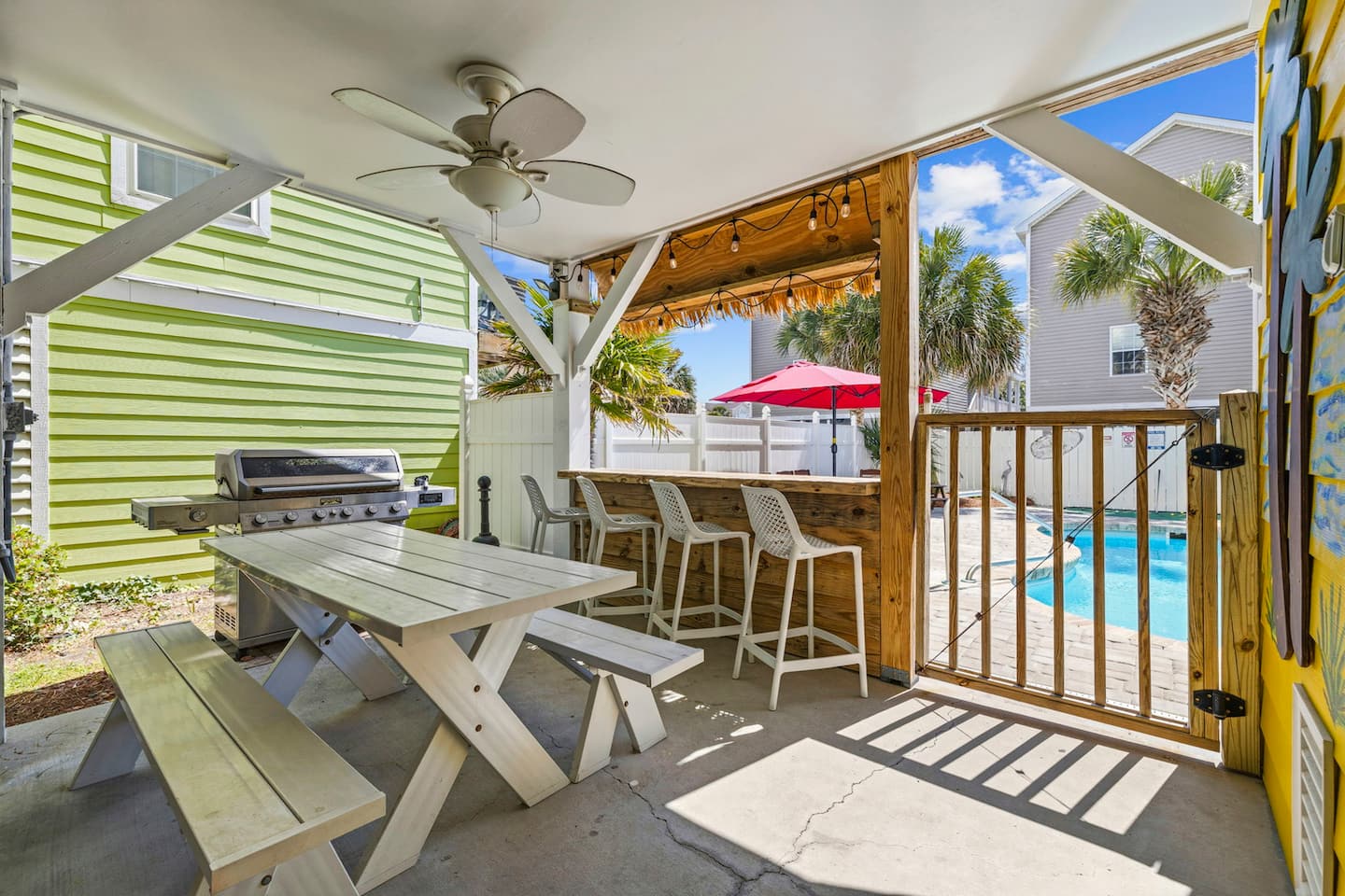 Fire up the gas grill under the covered carport. Propane provided, picnic table right there, tiki bar and pool visible just beyond the lattice.