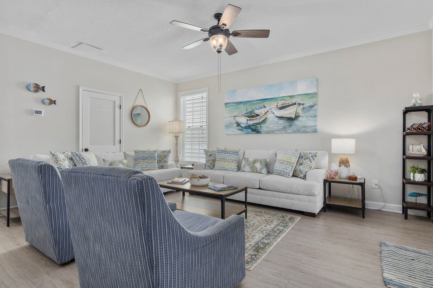 Find your seat. This angle shows the full living room layout with nautical boat painting on the wall, bookcase in the corner, room for everyone.
