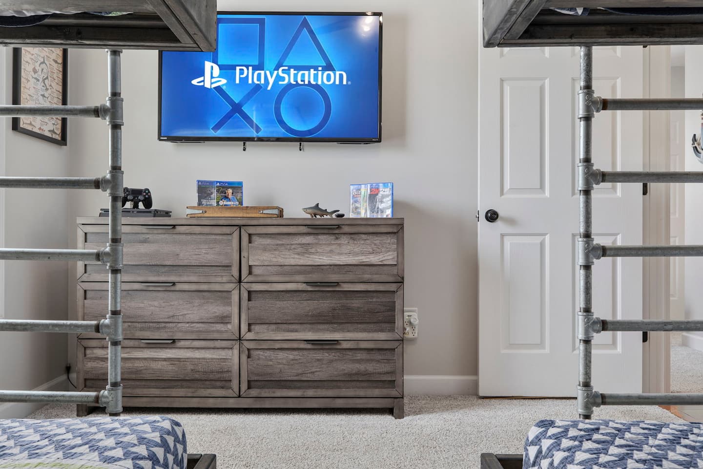 Watch the wall-mounted TV from the bunk. It sits right between the pipe-frame posts, so kids can game or stream without taking over the main screen.