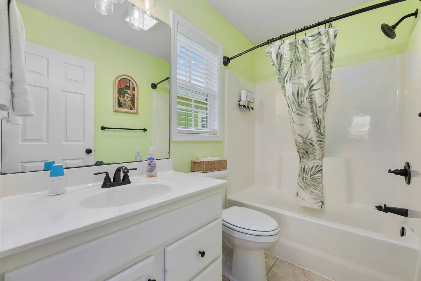 Rinse the salt off in the flamingo room's en-suite. Tub and shower combo with a tropical leaf curtain, white vanity, small colorful artwork above.