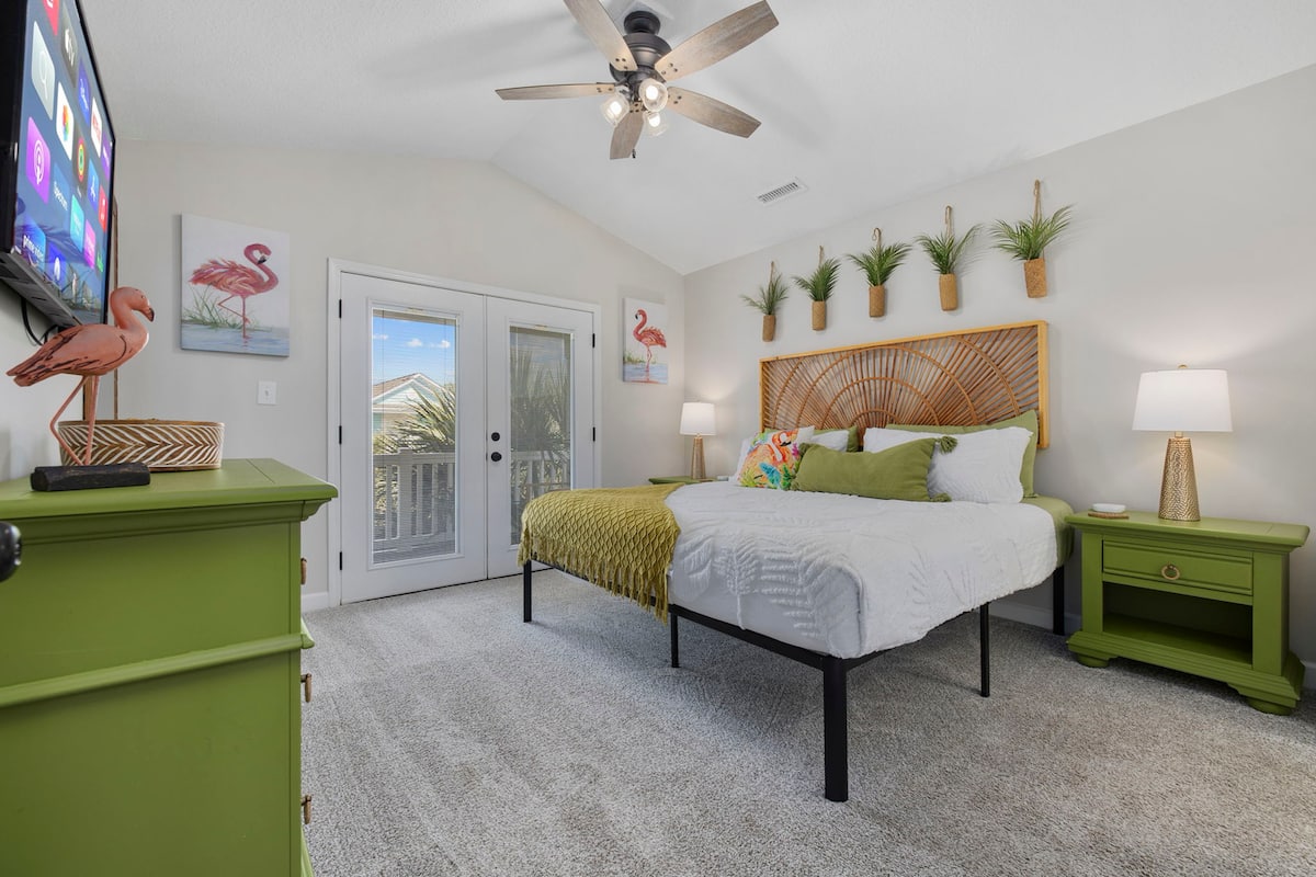 Wake up in the flamingo king room: rattan sunburst headboard, French doors to your private balcony, potted plants lining the wall shelf.