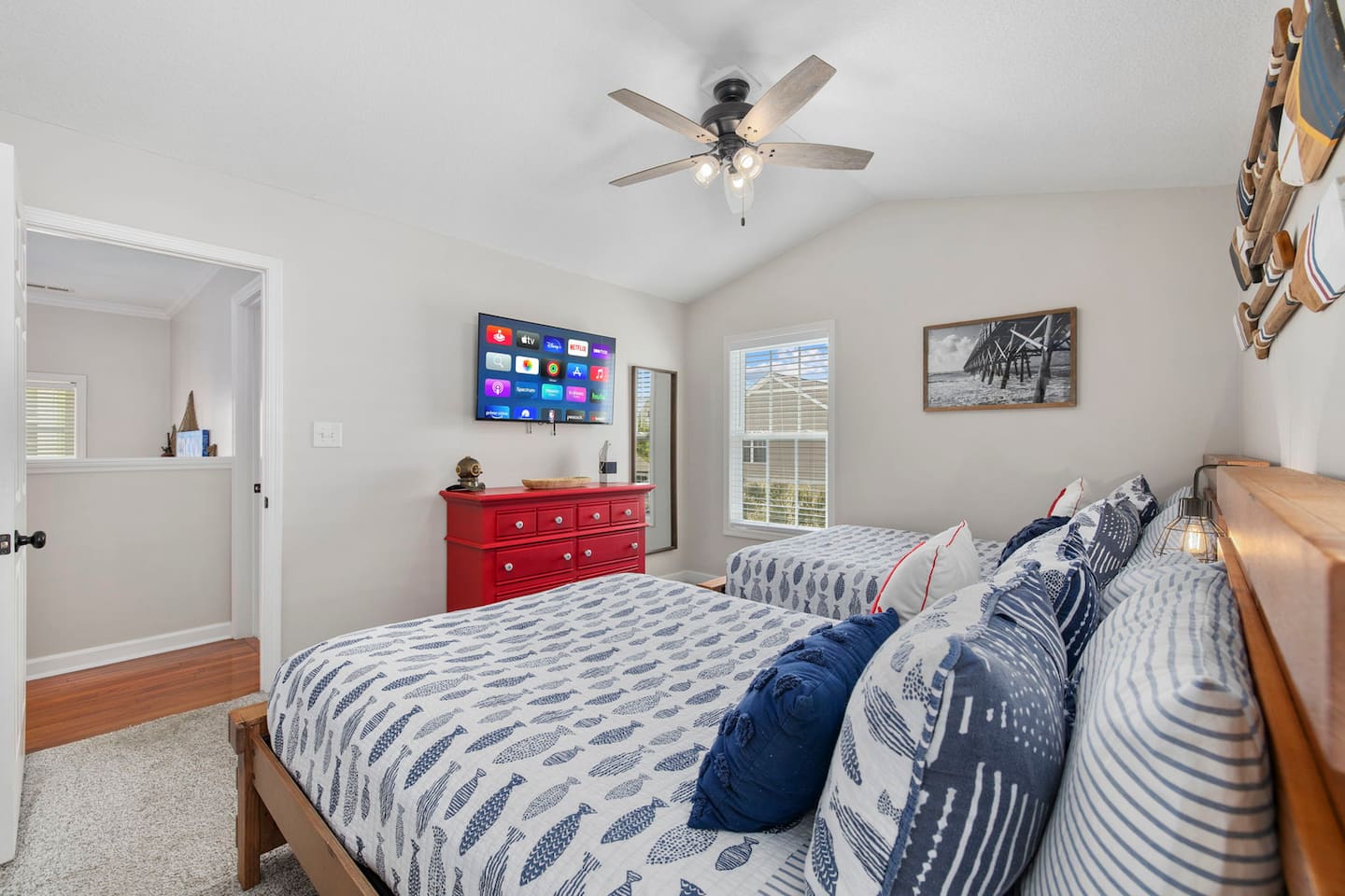 See both doubles clearly from this angle. Plenty of floor space between each bed, wall-mounted TV at the far end, dresser in the corner.