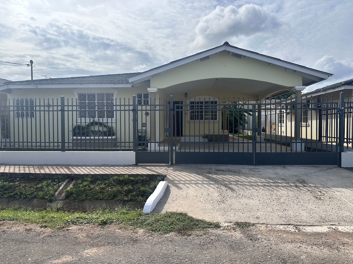 A spacious single-story house is highlighted by a welcoming front porch and large windows, allowing natural light to brighten the interior. The property is enclosed by a decorative metal fence, with a well-maintained lawn and driveway leading up to the entrance.