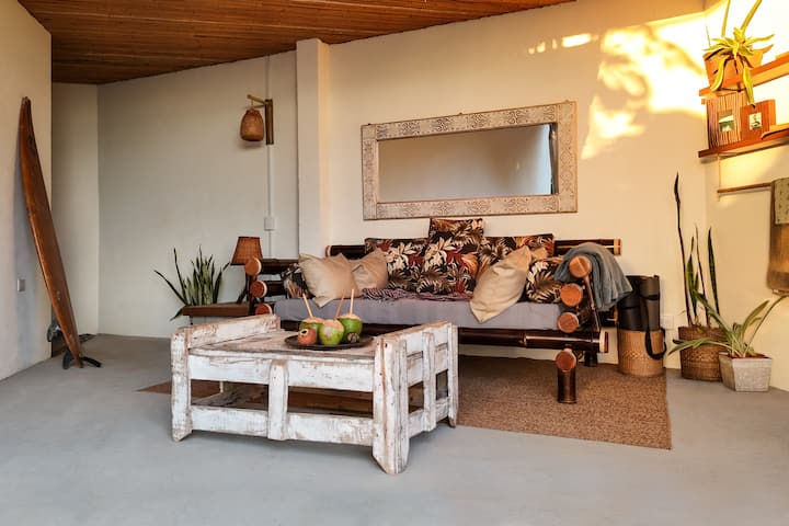 Lounge de reintegração à natureza semi-externo na entrada do chalé. Um santuário seguro e ao ar livre para rituais matinais. Para mais de 5 hóspedes, ele se transforma em um 3º quarto (sofá-cama de casal). Observação: sem banheiro privativo; os hóspedes compartilham as instalações das suítes com vista para o mar ou para a selva.