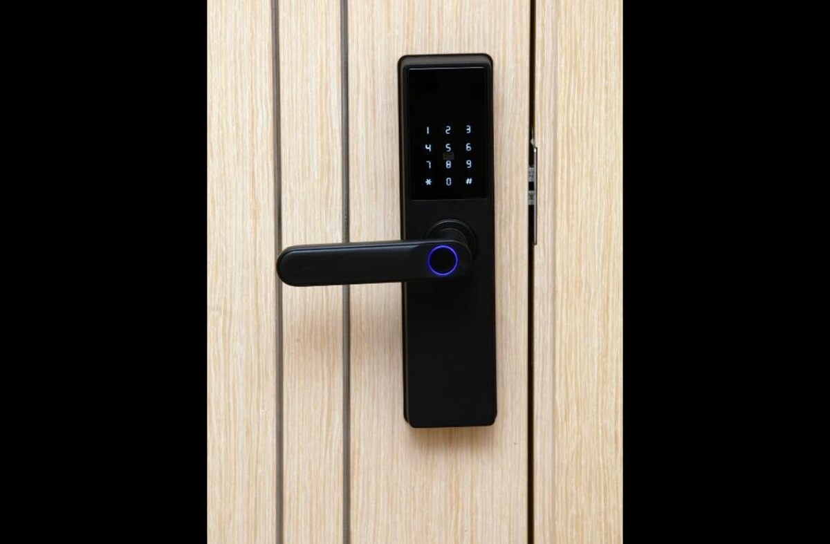 An electronic door lock is mounted on a wooden door. The lock features a digital keypad with illuminated numbers and a circular handle. Light wood grain adds a natural texture to the door's surface.