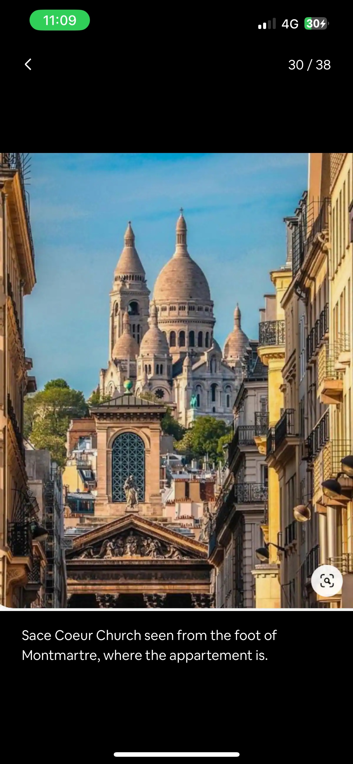 The image captures the iconic Sacré-Cœur Basilica atop Montmartre, framed by narrow, historic streets. The basilica's distinctive domes rise prominently against a clear blue sky, showcasing the architectural details of the surrounding buildings.