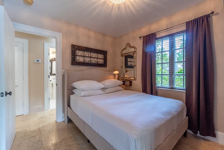 Chumba hiki cha kulala cha kupendeza kina kitanda cha kifahari cha kifahari, mapazia maridadi ya kahawia yaliyozimwa, na vioo vya kifahari vya mtindo wa zamani na kazi za sanaa.