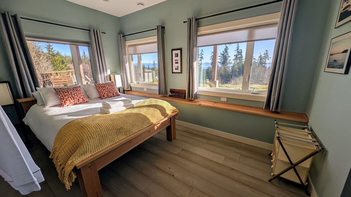 Dhomë gjumi e ndritshme dhe ftuese me dritare të mëdha me pamje të qetë nga oqeani dhe pylli