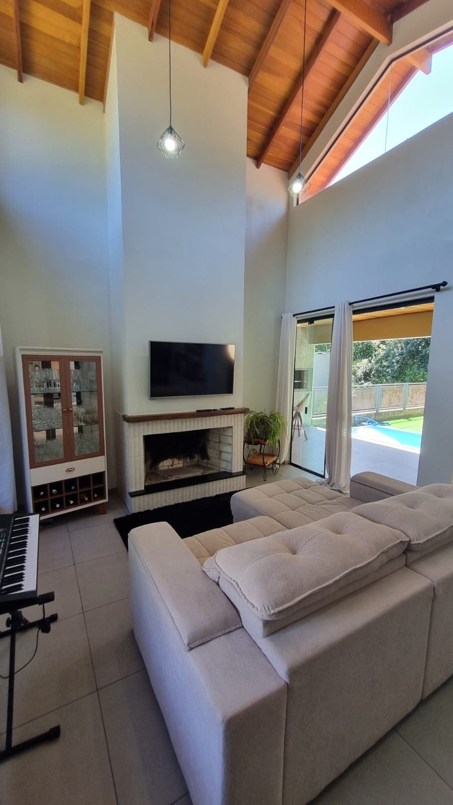 A bright living space is highlighted by a high ceiling and large windows that invite natural light. A plush seating area, positioned around a fireplace, offers a relaxing atmosphere. Nearby, a sliding glass door provides a view of the outdoor pool area.