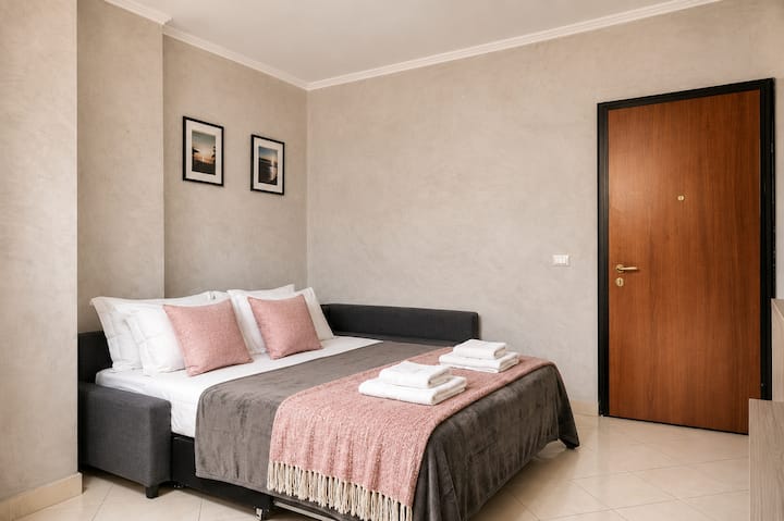 Sofá cama esquinero preparado en estilo de recámara doble, con sábanas blancas, cojines decorativos, una colcha a juego y toallas listas para los huéspedes. Una solución práctica, ordenada y acogedora para descansar con comodidad.