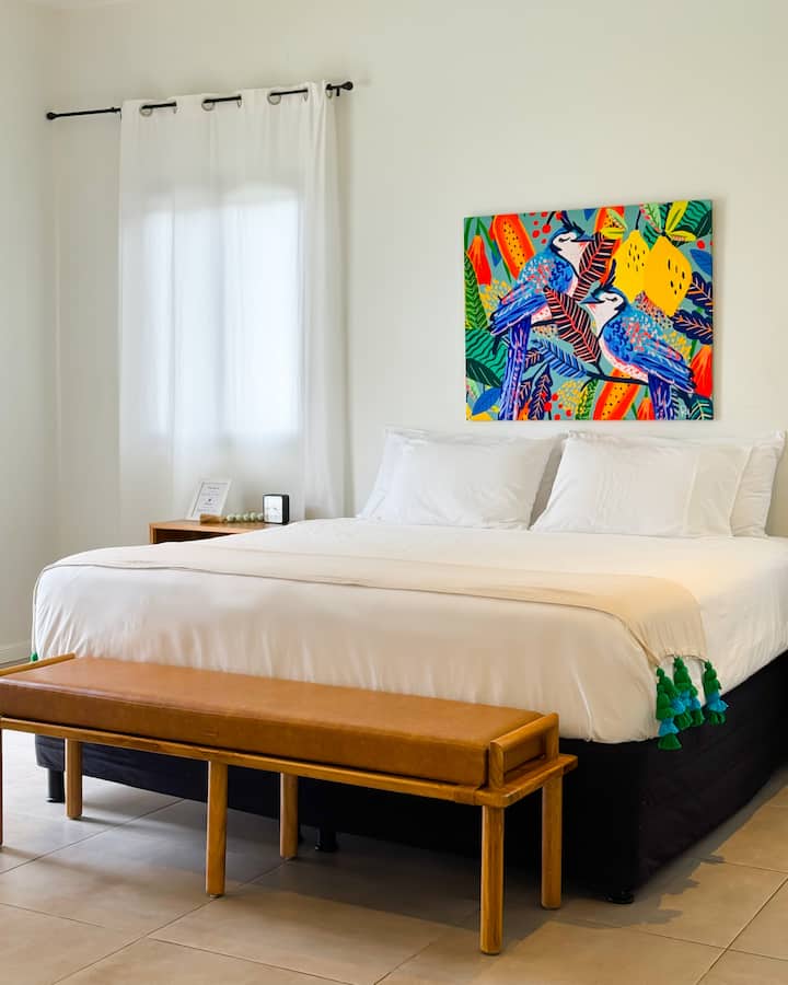 Nuestro espacioso dormitorio principal tiene una cama tamaño king Simmons, ropa de cama de algodón y está decorada con una canva hecha a medida “Urracas” de una talentosa ilustradora salvadoreña Raquel Arana.