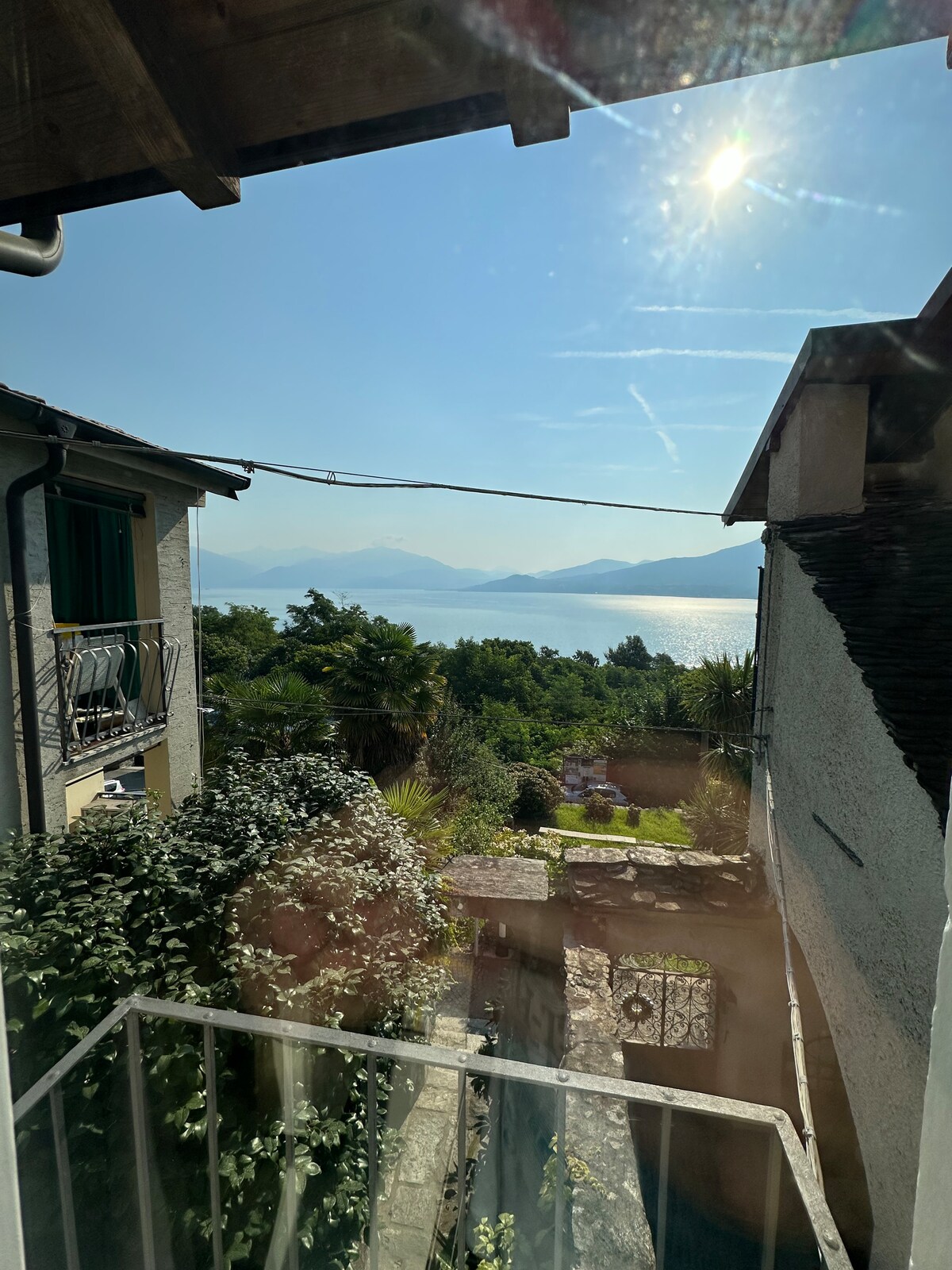 A serene view captures the shimmering waters of Lake Maggiore, framed by lush greenery and distant mountains. Sunlight reflects off the lake's surface, while the peaceful surroundings suggest a tranquil escape from busier locations.