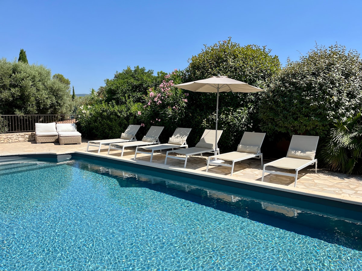 A private salt-water pool surrounded by a spacious terrace features six loungers and a shaded umbrella. Lush greenery lines the space, providing privacy and a serene atmosphere. The water is clear and inviting under bright blue skies.