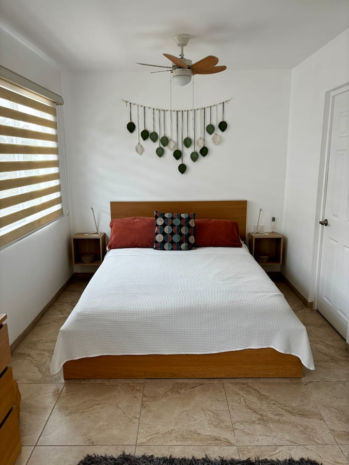 Camera da letto principale luminosa e silenziosa con letto matrimoniale, ventilatore a soffitto e spazio per riporre gli effetti personali.