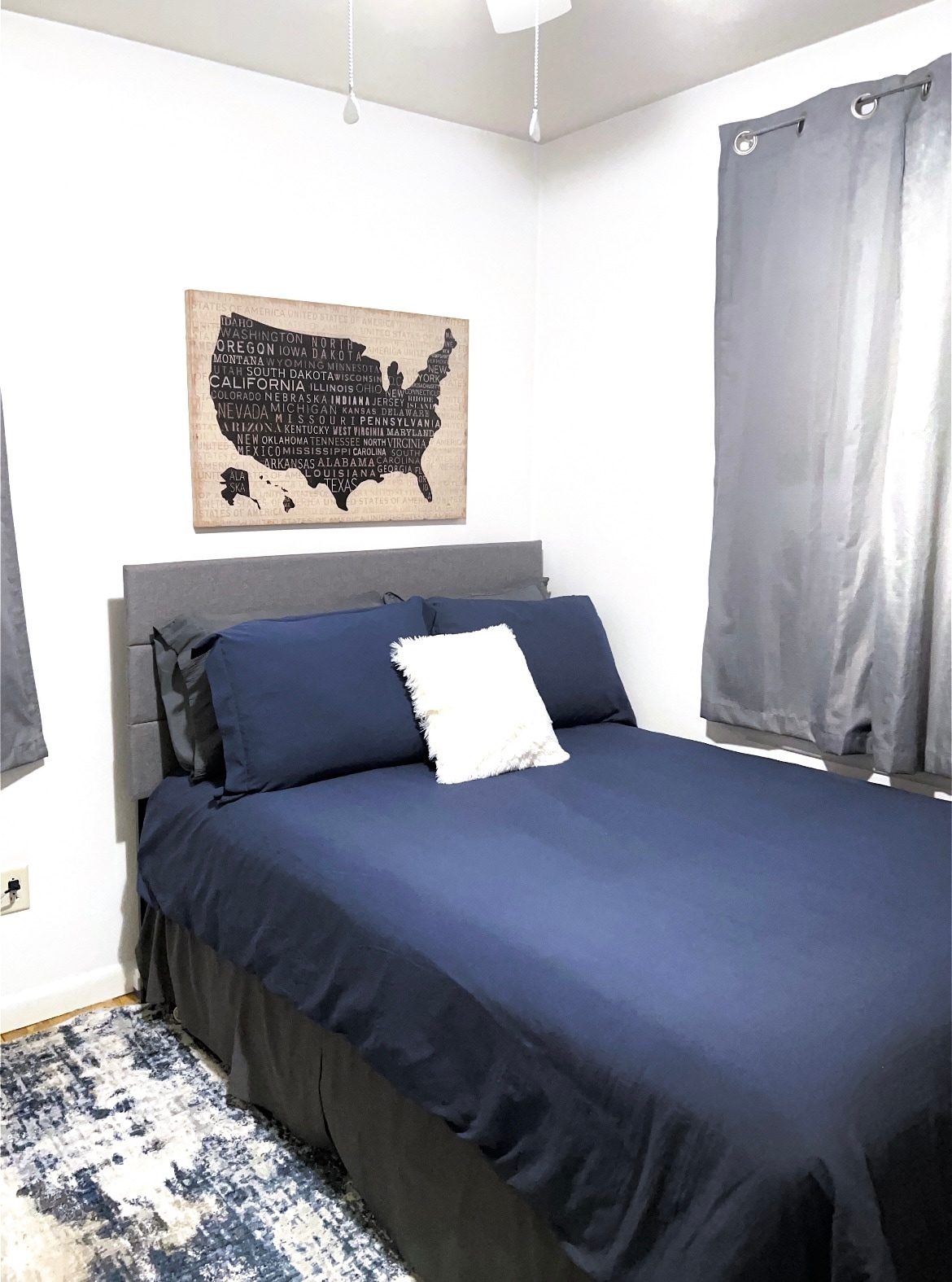 Dormitorio azul y gris con toques de naturaleza y decoración de viajes. Esta habitación cuenta con una cama doble, cortinas opacas y ventilador de techo para dormir cómodamente. 