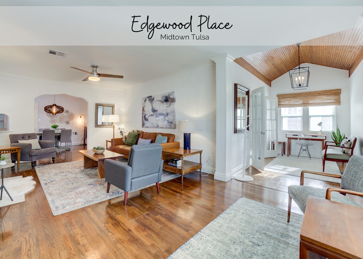 An inviting living area features hardwood floors and a variety of seating options, including chairs and a sofa. Natural light fills the space through multiple windows, with a view of a bright workspace. A tasteful area rug adds warmth to the room.