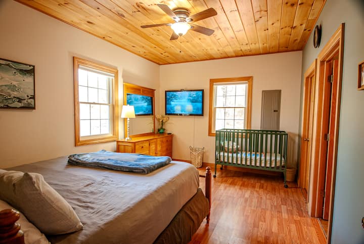 The master bedroom features a king bed, private en-suite bathroom, room-darkening shades, and Roku TV. Toiletries, bed linens, and bath towels are included. A full-size crib is available upon request.
