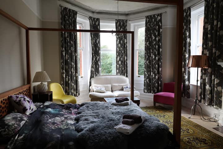 Dette enorme, luksuriøse dobbeltværelse har en smuk udsigt over haven. Den har en sofa, fløjlsstol, stort indbygget klædeskab, kommode og sengeborde med lamper, en dobbelt himmelseng og en smuk original pejs.
