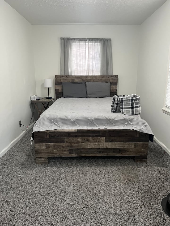 Chumba kikubwa cha kulala chenye nafasi kubwa chenye mwanga wa asili, kilicho na kitanda thabiti cha kijijini, meza kando ya kitanda, taa, feni na televisheni mahiri ya inchi 32. Zulia laini na sauti zisizoegemea upande wowote huunda hisia ya starehe.  Bafu bora hatua chache tu zinaongeza urahisi na utendaji.