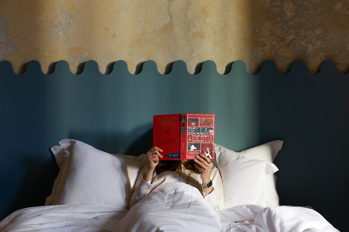 Double room, with original cement floor and Raw beauty style walls. In the center of the room is a large bed with a modernist-style wave headboard, designed by the hosts for Collezione Caleido. 
