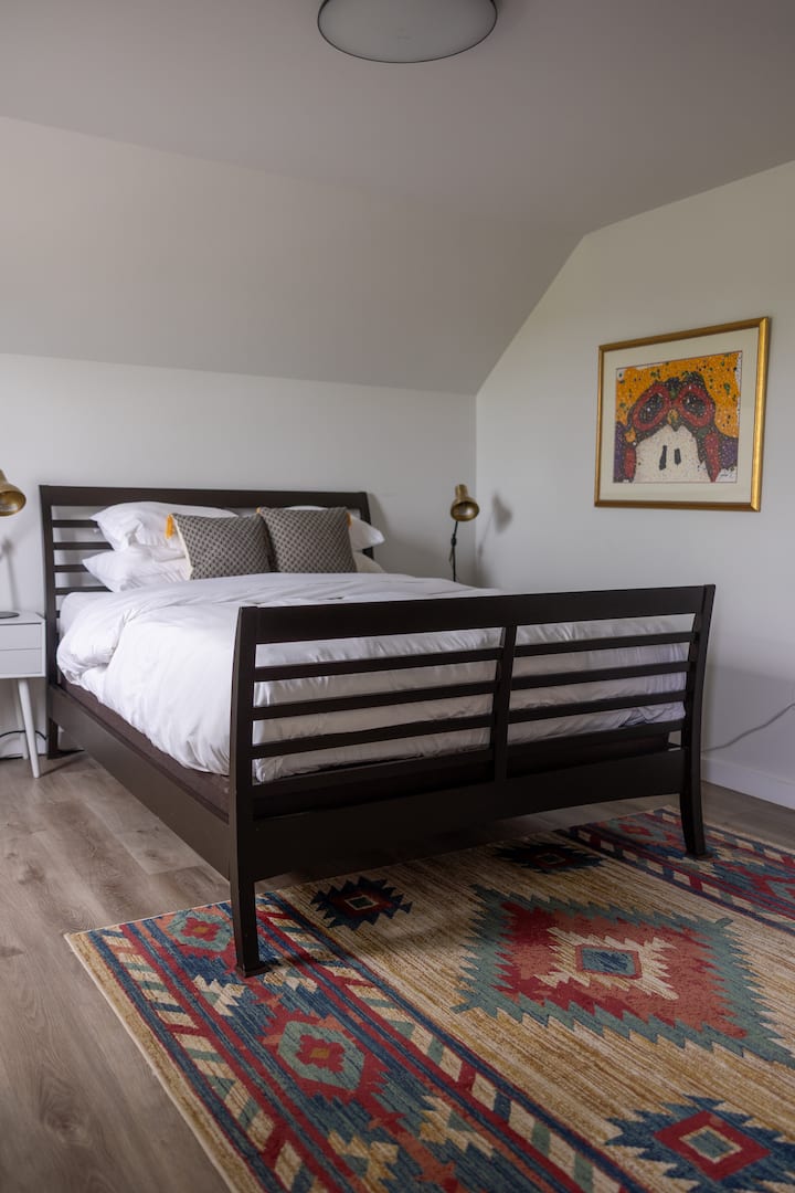 Cozy bright bedroom with stylish rug, artwork, and crisp white linens
