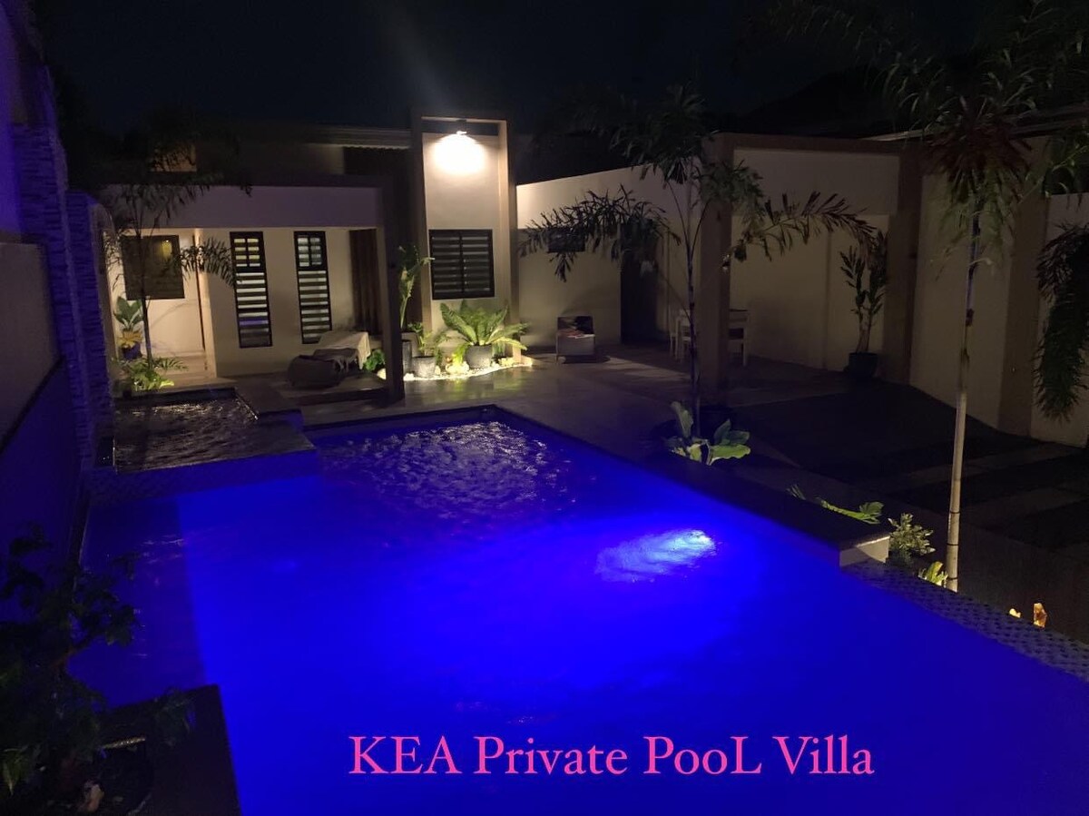A serene private pool is illuminated in calming blue tones, surrounded by lush greenery. The villa features a minimalist design with smooth stone pathways leading to cozy seating areas, enhancing the tranquil evening atmosphere.
