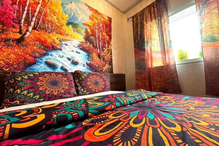 Chambre lumineuse et chaleureuse au décor vibrant, dotée d'un lit double confortable, de draps colorés et d'une superbe œuvre d'art représentant la nature. Profitez de la lumière naturelle grâce aux grandes fenêtres, du mobilier en bois élégant et d'une atmosphère chaleureuse et accueillante, parfaite pour se détendre