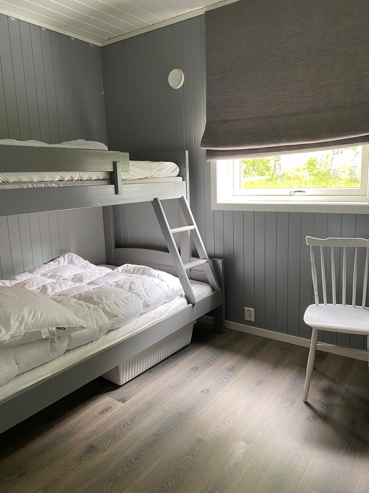 Dormitorio en el primer piso con ventana orientada al amanecer, abedules y zona exterior con bancos. 