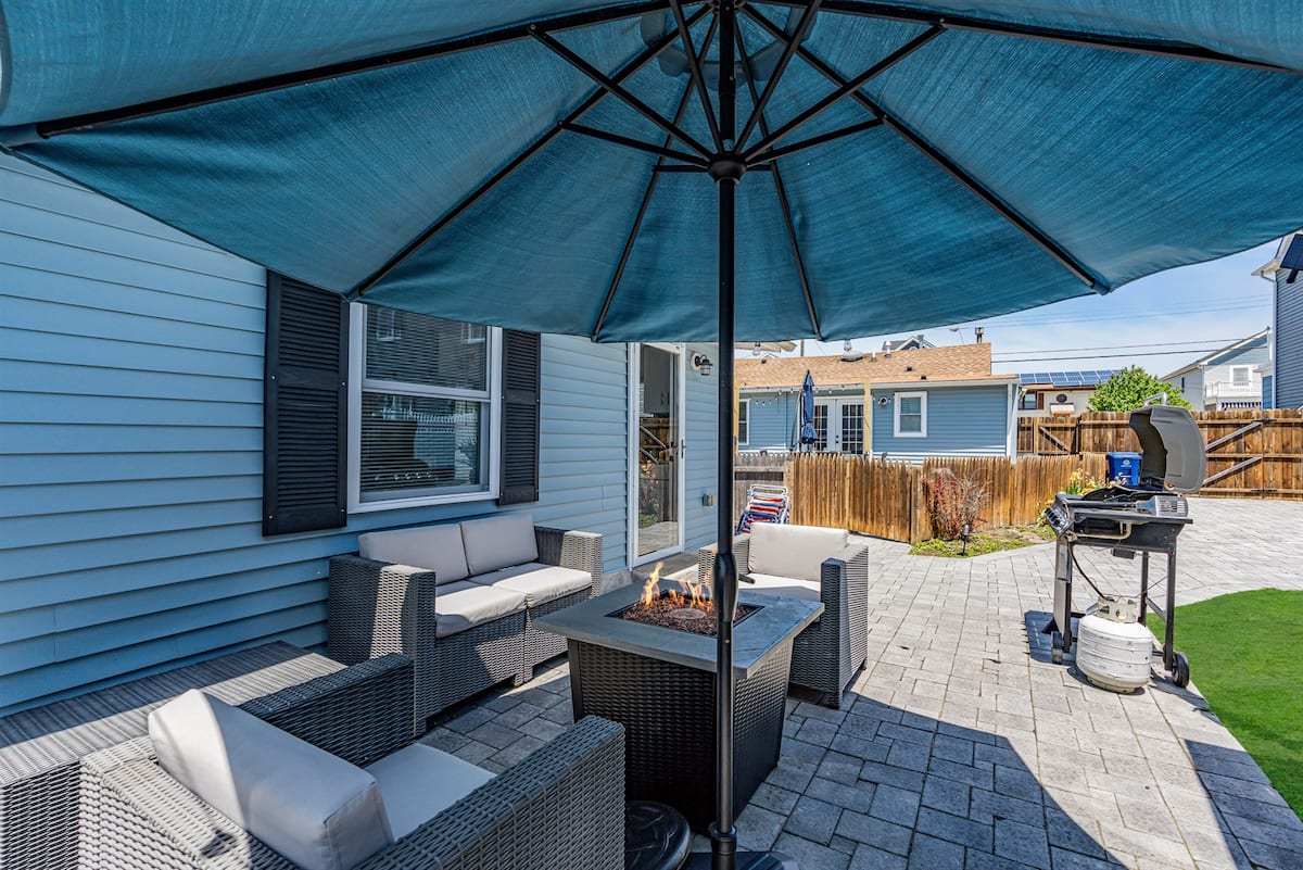 The paver patio at golden hour with a lit fire pit table, umbrella and string lights