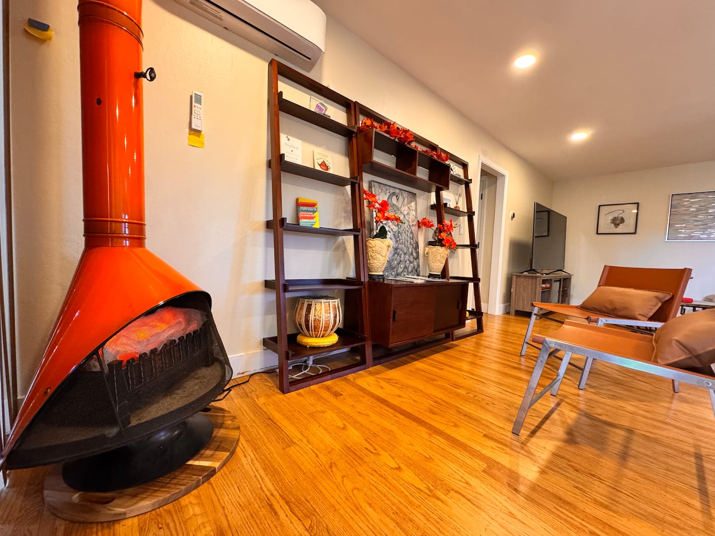 Orange mid-century fireplace beside sculptural chairs and open shelving
