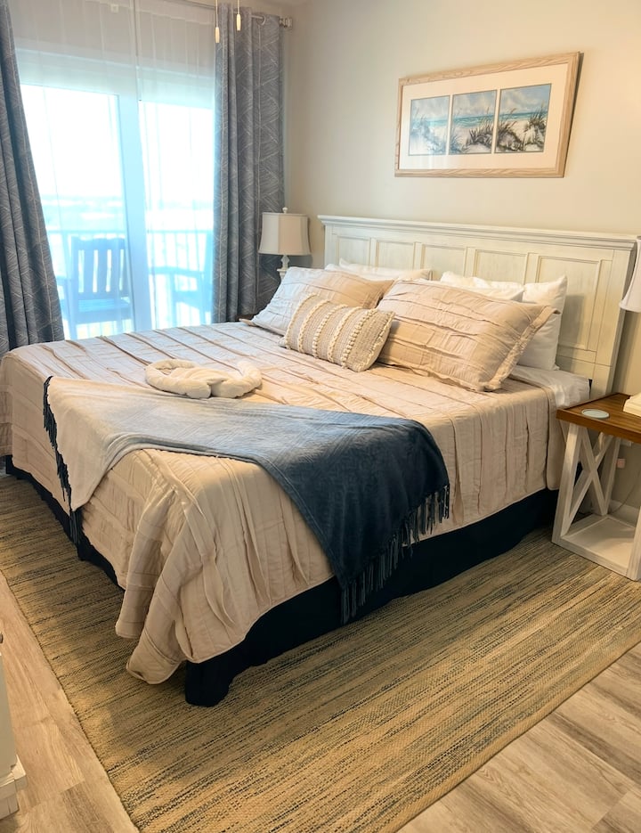 Master bedroom with a BRAND NEW king bed with memory foam mattress, ceiling fan, floor fan, access to balcony, Roku TV, dresser and full length mirror.