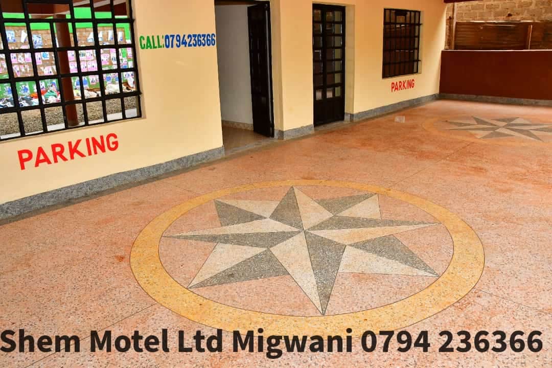 An open courtyard features a colorful tiled floor with a star pattern, surrounded by walls that have large windows. The space is well-lit and provides clear signage for parking. The area is accessible and offers a welcoming atmosphere.