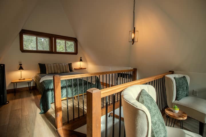 A queen bed, sitting area, luggage rack and two floor fans are in the loft area.