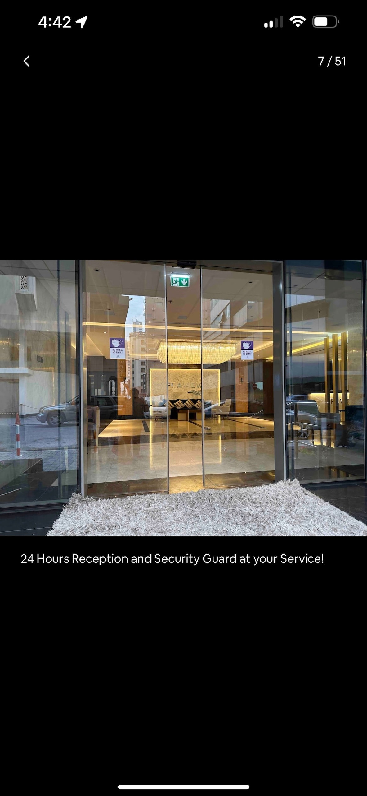 The entrance features large glass doors that invite guests into a welcoming lobby adorned with modern furnishings. Soft lighting enhances the open space, highlighting smooth flooring and comfortable seating arrangements. A reception area is visible, offering 24-hour service for guests.