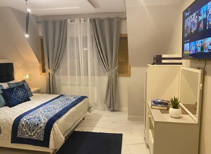 غرفة نوم هادئة تتميز بألوان زرقاء باردة وأرضيات على طراز الرخام وإضاءة ناعمة. تجمع هذه المساحة الراقية، المثالية لقضاء ليالٍ مريحة، بين الأناقة الحديثة والأجواء الهادئة والمتجددة الهواء.