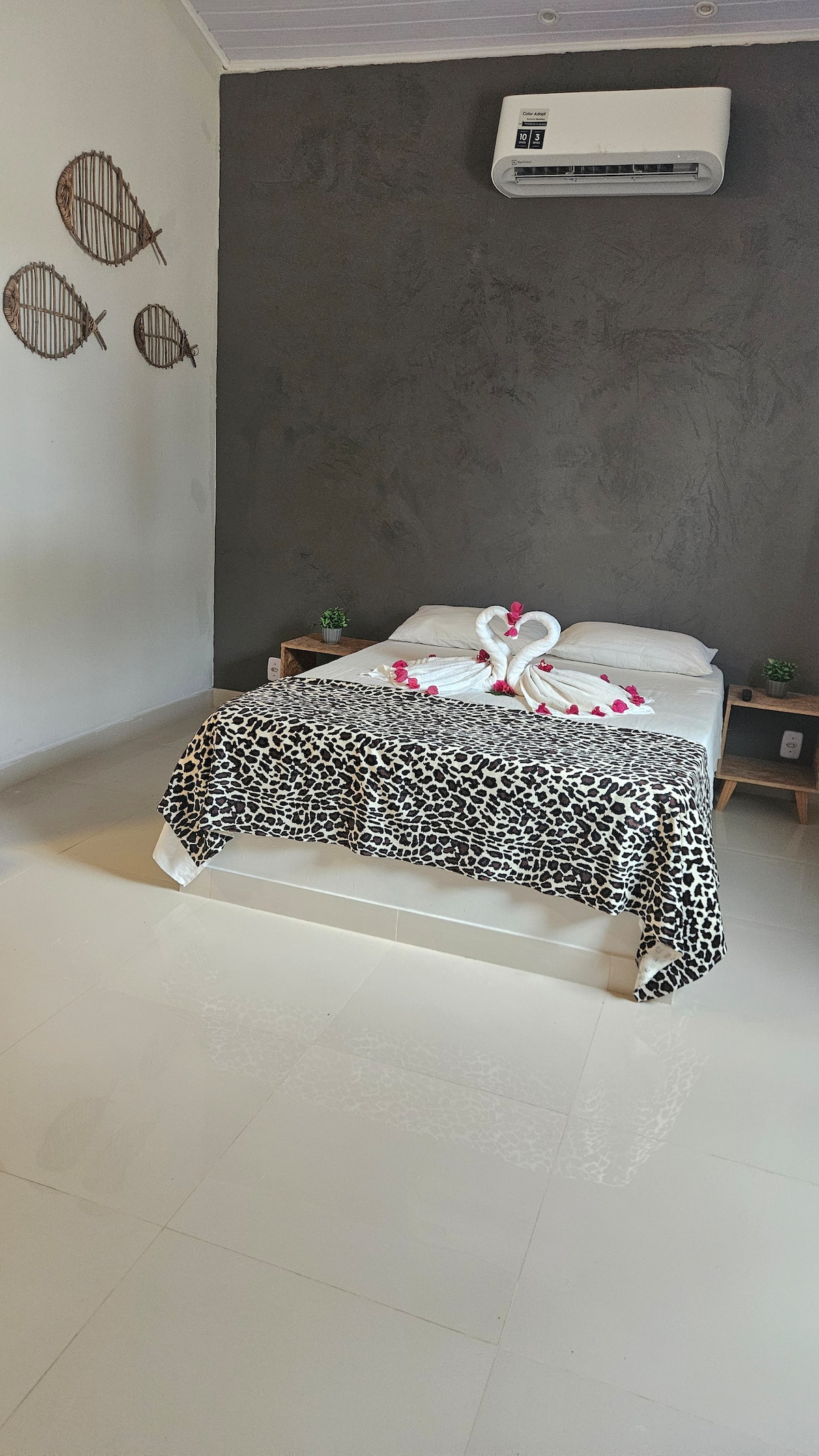 A sleeping area features a spacious bed decorated with a black and white leopard print blanket. Elegant towel swans are arranged at the foot of the bed. Soft lighting illuminates the room, highlighting the textured gray wall and decorative wall art.
