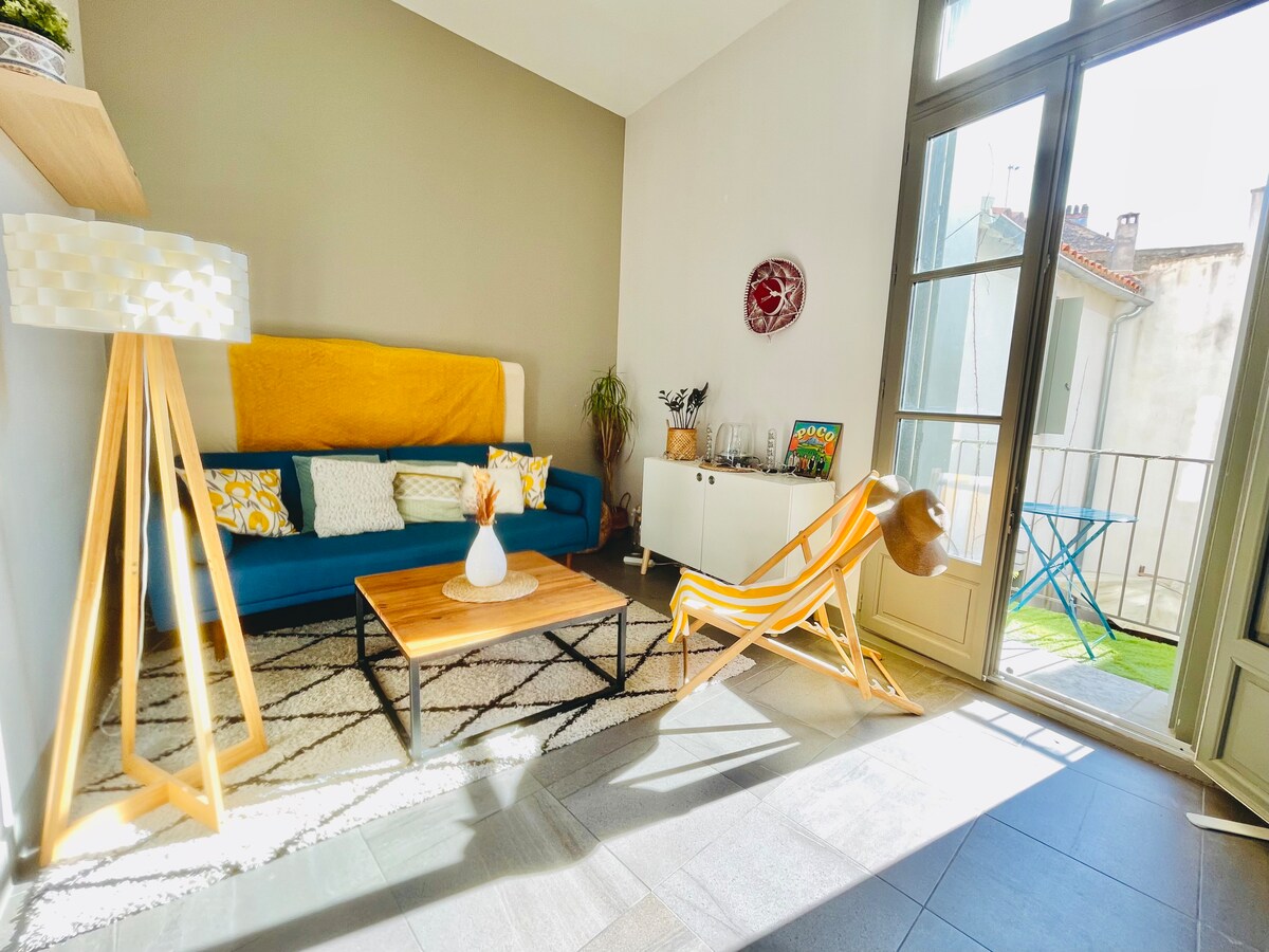 A bright living area is showcased, featuring a blue sofa adorned with decorative pillows, a wooden coffee table, and an indoor plant. Natural light floods the space through large glass doors that open to a small balcony, enhancing the inviting ambiance.