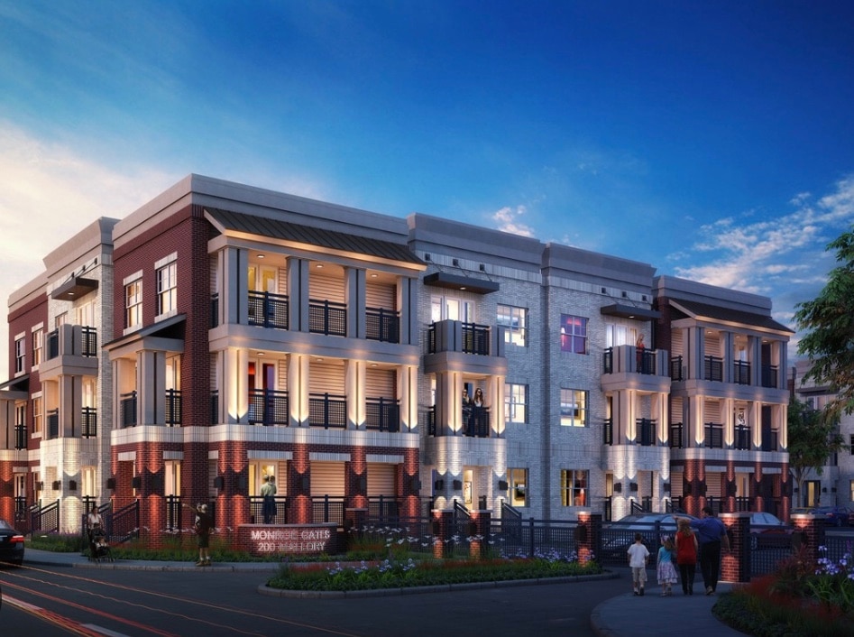 A modern multi-story building is showcased, featuring a combination of red brick and light stone exteriors. Balconies adorned with black railings are visible on each floor, framed by large windows. The sky transitions to twilight, illuminating the structure in soft evening light.
