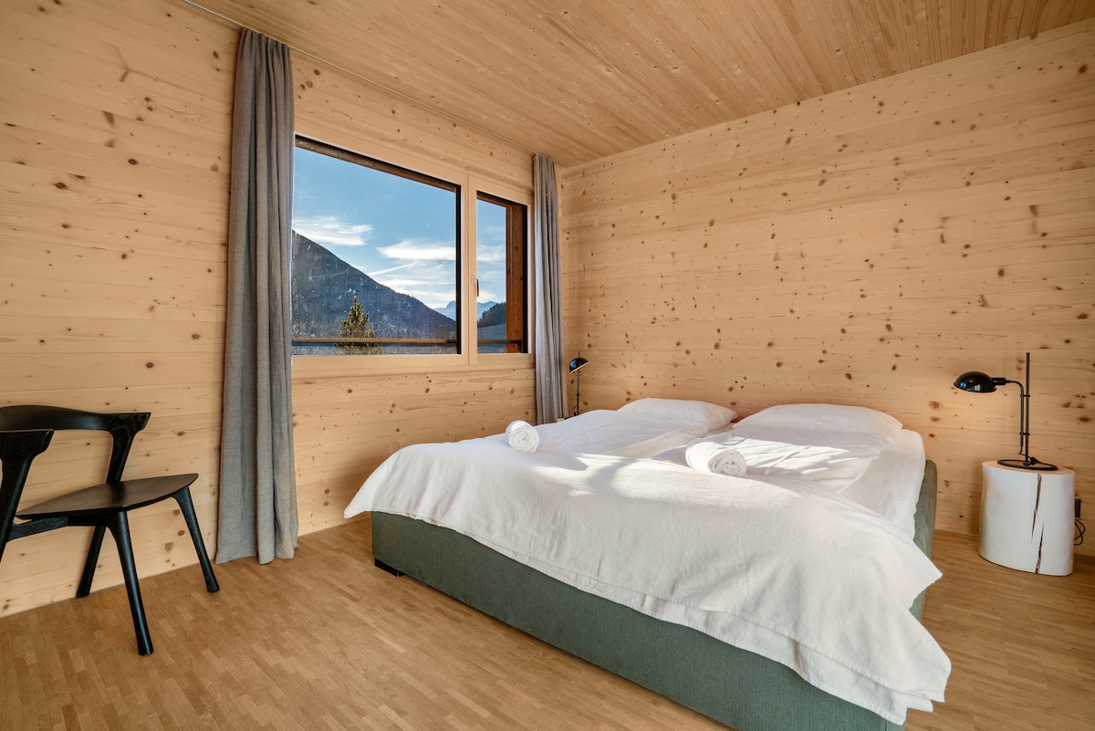 Dormitorio luminoso con cama doble grande, toallas limpias y vistas a la montaña desde la ventana.