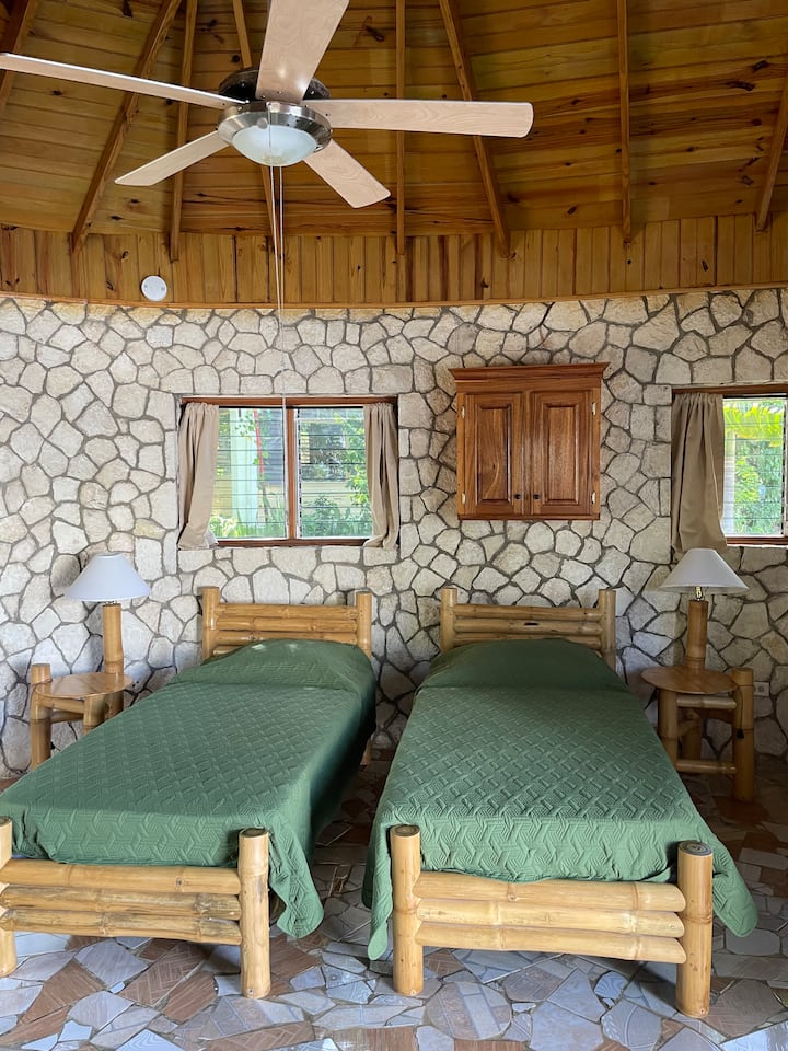 Ორი ბამბუკის ტყუპი საწოლი ამ ქვის სახლში. Აპარტამენტის საძინებელი. ჭერის ვენტილატორი. Კონდიციონერი არ არის.  პირდაპირ შედიხართ აუზის ტერასაზე. 