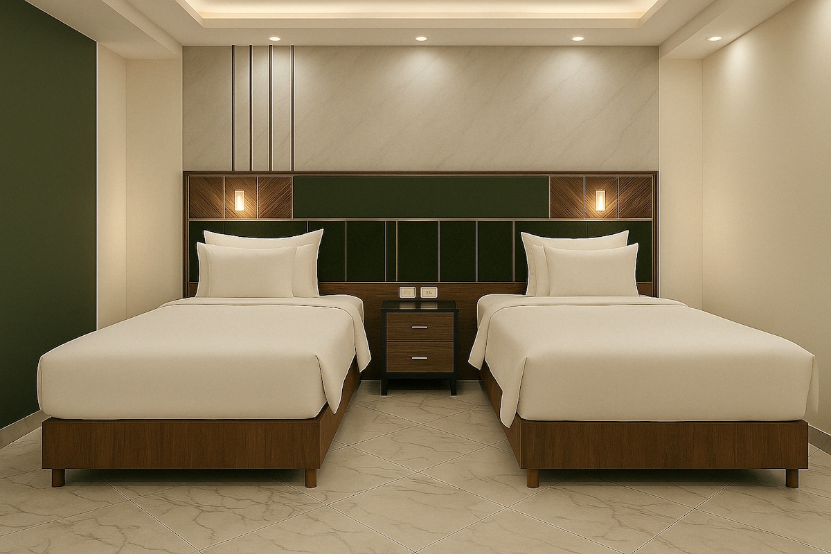 A well-appointed bedroom featuring two spacious beds with light-coloured bedding. A modern nightstand is positioned between the beds, showcasing a minimalist design. The walls are accented with a dark green panel, complemented by soft, ambient lighting that enhances a sense of comfort.