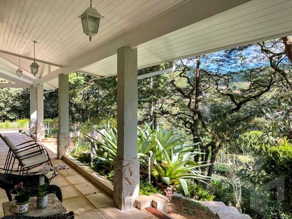 A spacious porch is flanked by potted plants and features comfortable loungers. Lantern-style light fixtures hang from the ceiling, and the surrounding lush greenery offers a serene view of the natural landscape beyond.