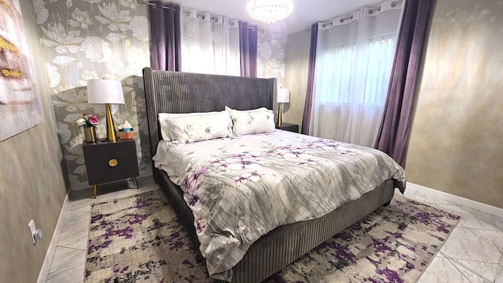 Deuxième chambre confortable dans des tons violet et or avec un lit king size, 2 tables de chevet et des lampes. La chambre a un placard. Le lustre se transforme en ventilateur.