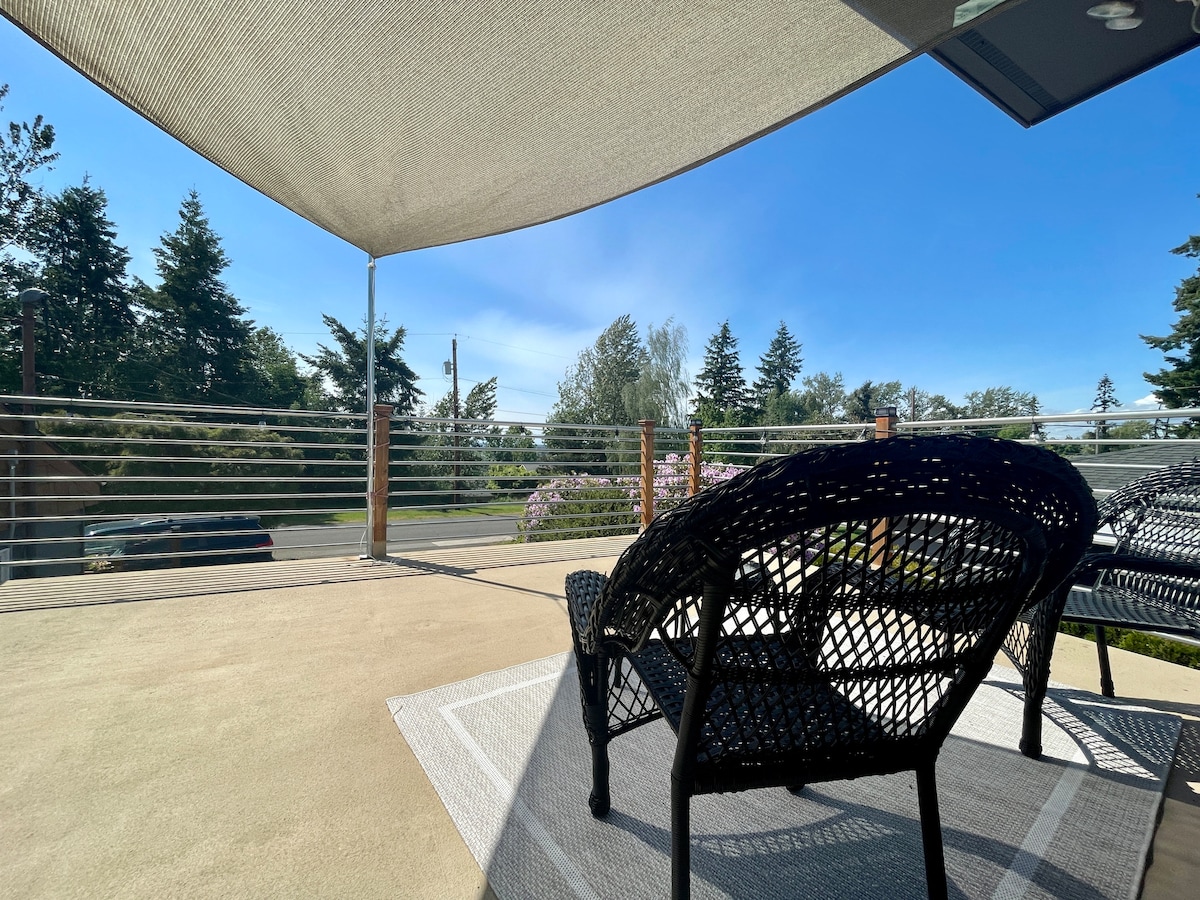 An elevated deck is showcased, featuring comfortable seating arrangements with woven chairs. A sunshade provides coverage from sunlight, while views of greenery and distant trees are visible in the background. The space is designed for relaxation, with ample room to enjoy the outdoors.