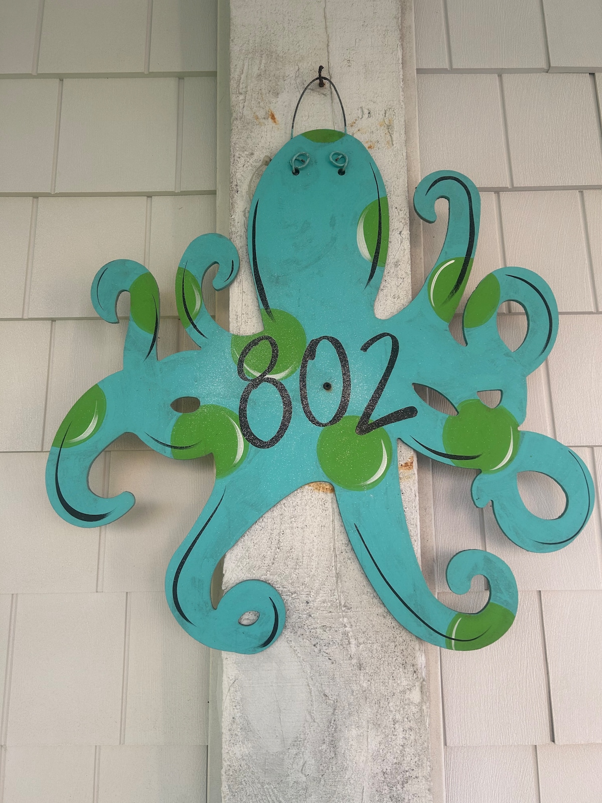A large, textured wooden octopus sign hangs on a wall, featuring a bright turquoise color with green accents. The number '802' is prominently displayed in the center, adding a playful touch to the decor.